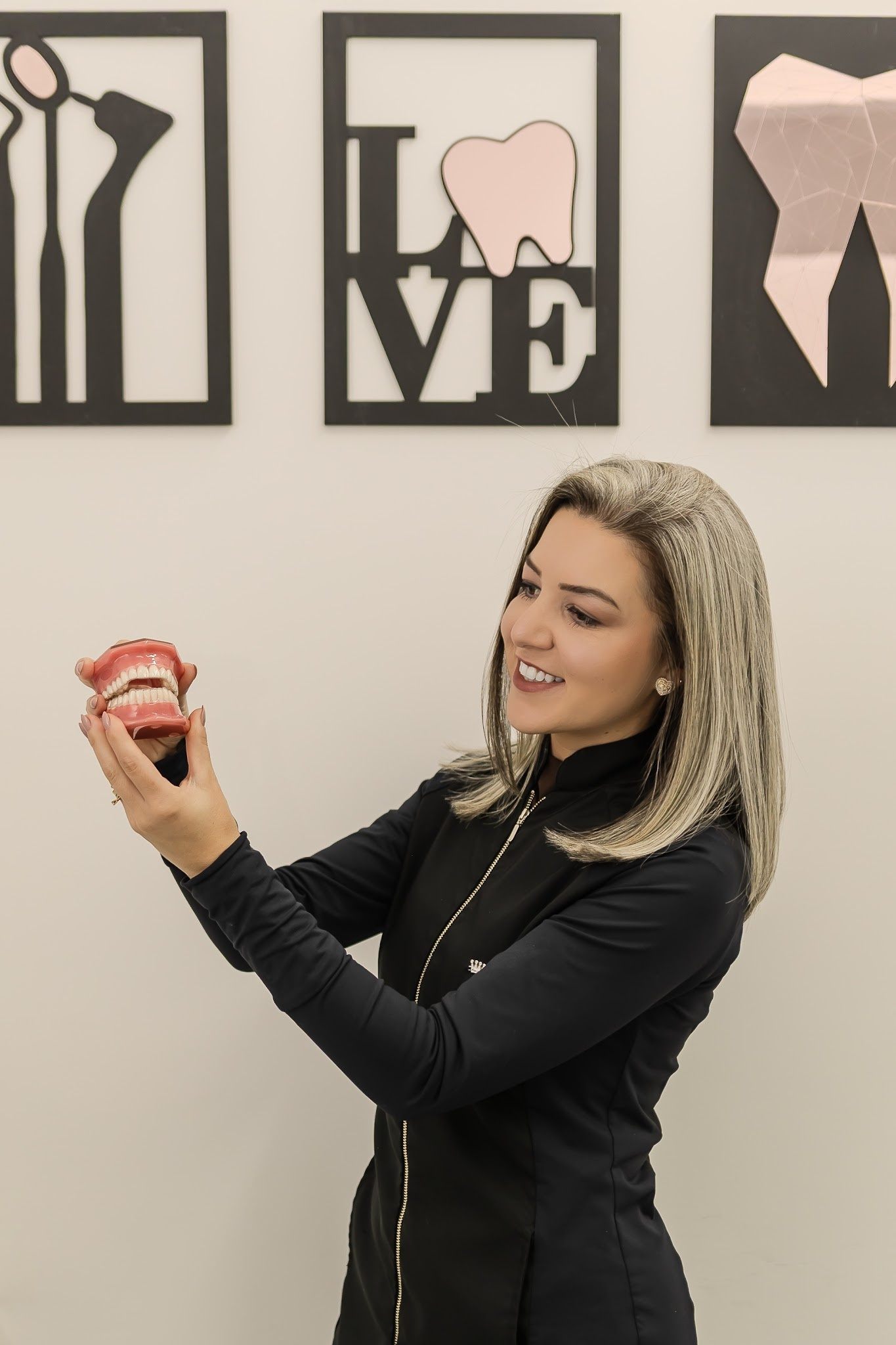 Dentista mostrando modelo de arcada em frente aos quadros LOVE